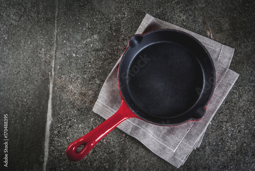Cooking food background. Empty red cast iron frying pan with a towel on a black stone table, top view copy space