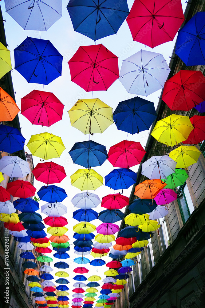 Fototapeta premium Colorful umbrellas background. Coloruful umbrellas urban street decoration. Hanging Multicoloured umbrellas over blue sky.
