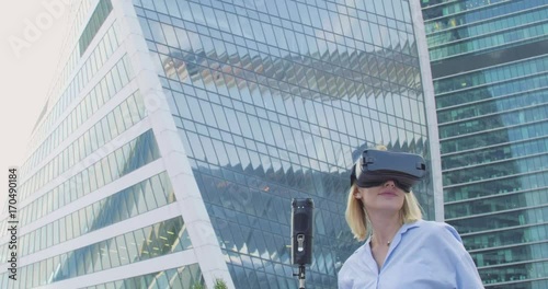 A blond woman in a blue shirt with a VR glasses and camera 360. Skyscrapers are on the background 4K