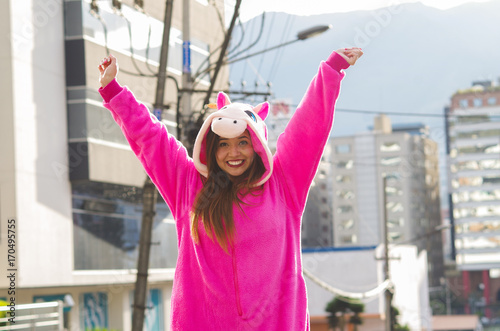 Close up of a beautiful smiling young woman wearing a pink unicorn costume, with both hands up at outdoors in the city of Quito