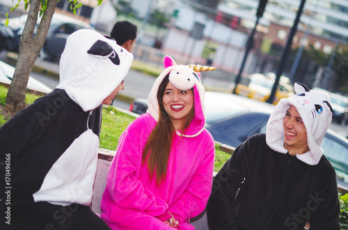 Close up of a happy group of friends having a fun conversation and wearing different costumes, one woman wearing a pink unicorn costume, other woman a panda costume and the man wearing a cat costume