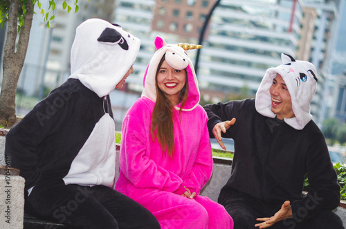Close up of a happy group of friends having a fun conversation and wearing different costumes, one woman wearing a pink unicorn costume, other woman a panda costume and the man wearing a cat costume