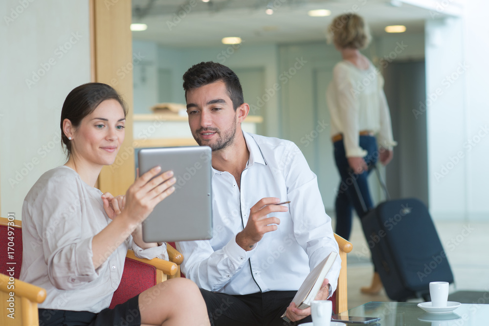Obraz premium couple sitting in hotel lobby looking at digital tablet