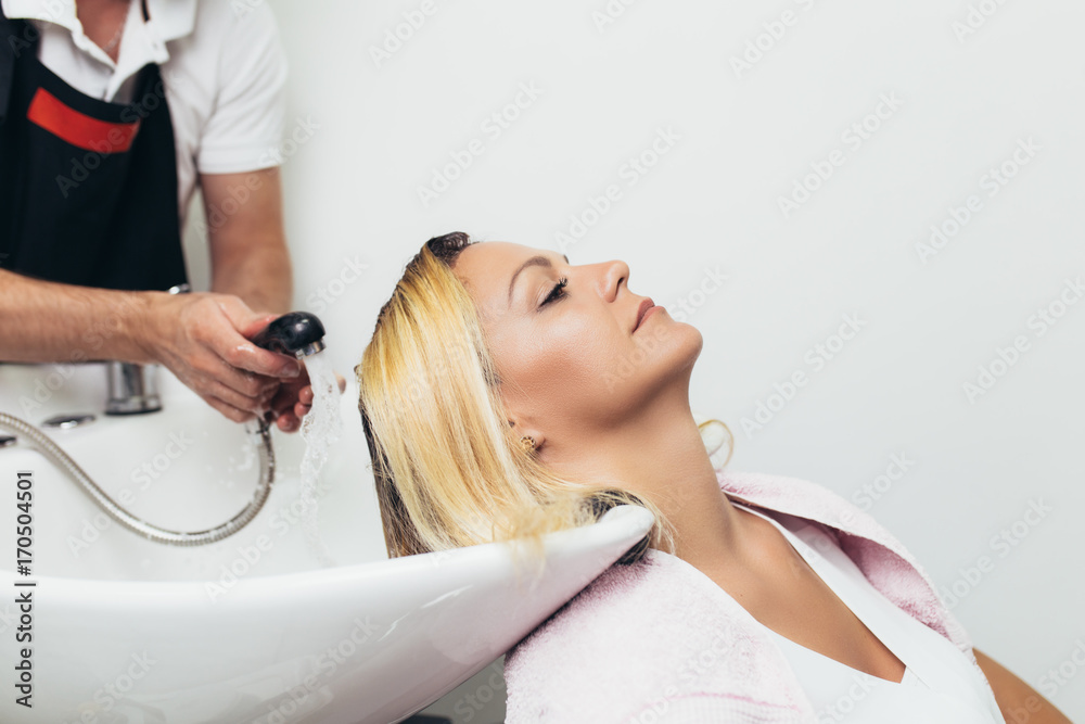 Naklejka premium Hairdresser washing hair of a beautiful woman in hair salon.