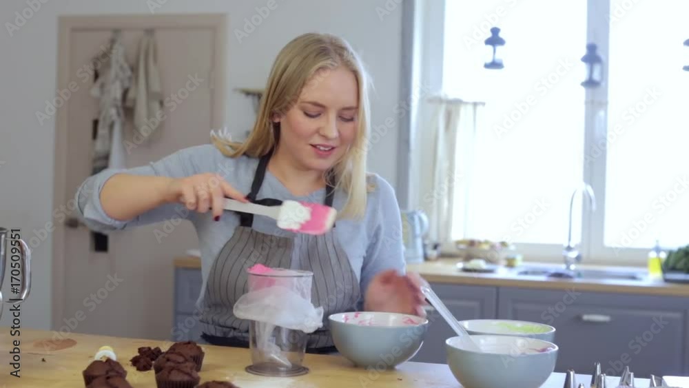 Blonde female making cream for decorating cupcakes, doing hobby. Woman puts the cream in pastry bag using a spatula. Blonde female making cream for decorating cupcakes, doing hobby. Woman puts the cream in pastry bag using a spatula.