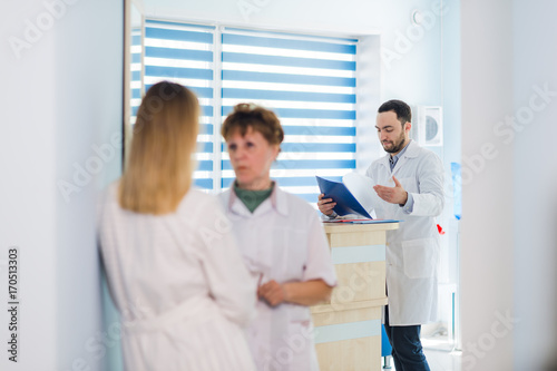 Mature doctor discussing with nurses in a hallway hospital. Doctor discussing patient case status with his medical staff after operation.