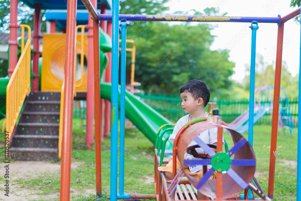 Fototapeta premium Sad little Asian kid at the playground under the sunlight in summer, shallow DOF