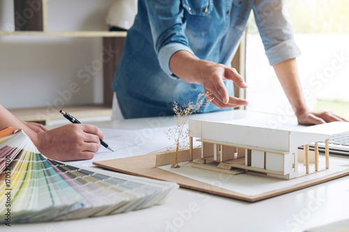 Two young women interior design or graphic designer working on project of architecture drawing with work tools and color swatches, colour chart in digital tablet at workplace