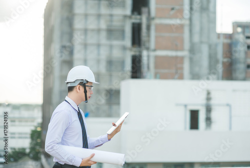 smiling young architect or engineering builder in hard hat with tablet over group of builders at construction site, architect watching some a construction, business, building, industry, people concept