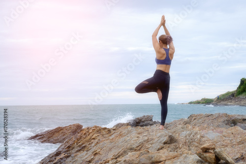The woman practicing yoga on the beach at sunset.