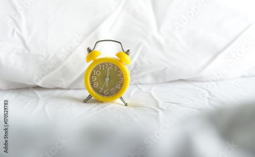 Yellow Alarm clock on bed in morning with sun light photo