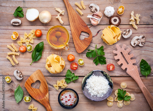 Italian foods concept and menu design. Fettuccine with wooden spatula and ingredients sweet basil ,tomato ,garlic ,parsley ,champignon and extra virgin olive oil setup on wooden background.