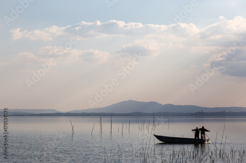 Two fishermen on a little boat with a fishing net, with beautiful warm tones and distant sun rays