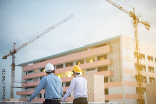 Smiling young architect or engineering builder in hard hat with tablet over group of builders at construction site, architect watching some a construction, business, building, industry, people concept