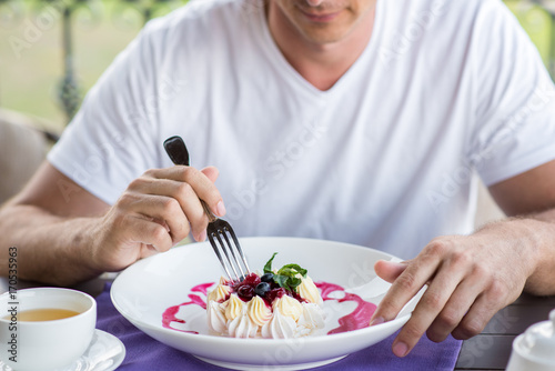 Handsome young man eating with a fork cake Pavlova