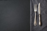 Rustic gray linen napkin, silverware and black slate dish with copy space for your menu or recipe. Menu card for restaurants. Top view.