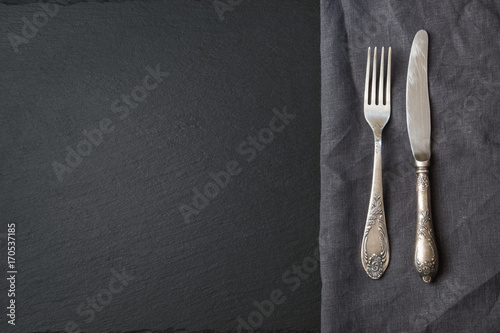 Rustic gray linen napkin, silverware and black slate dish with copy space for your menu or recipe. Menu card for restaurants. Top view.
