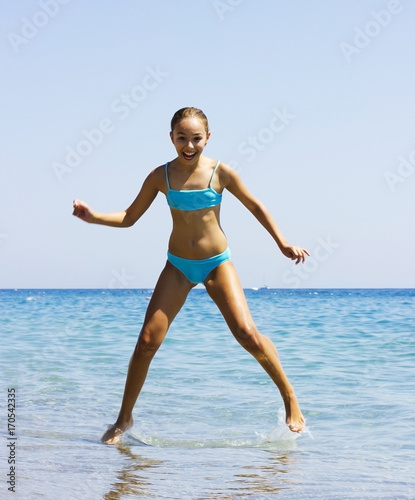 Young pretty smiling girl in blue swimsuit jumping into the sea on the beach