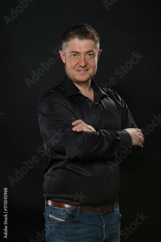 Young confident man portrait of a confident businessman showing by hands on a black background. Ideal for banners, registration forms, presentation, landings, presenting concept.