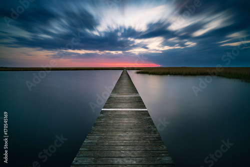 Old wooden pier on calm lake at sunset