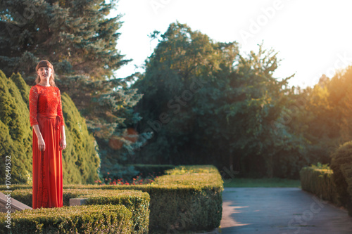 Beautiful young girl in a long red dress in an autumn park. photo