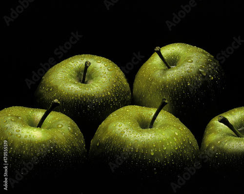Fresh green apples covered in water droplets on black background