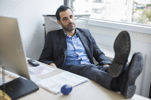 Manager seduto comodamente nel suo ufficio, con i piedi sopra la  scrivania tiene il telefono in una mano e un antistress nell'altra con aria di attesa photo