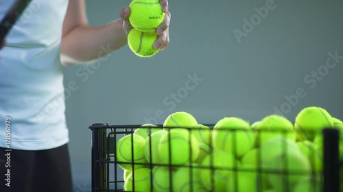 Balls for big tennis in the basket: Tennis player takes three balls from basket, then one throws it back. Sports equipment for playing tennis. Hands of a tennis player with a racket. Close-up. photo