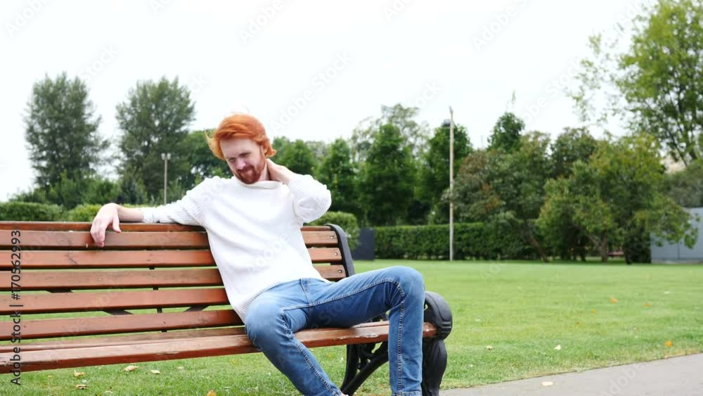Tired Man with Neck Pain, Red Beard and Hairs, Sitting in Park on Bench Tired Man with Neck Pain, Red Beard and Hairs, Sitting in Park on Bench