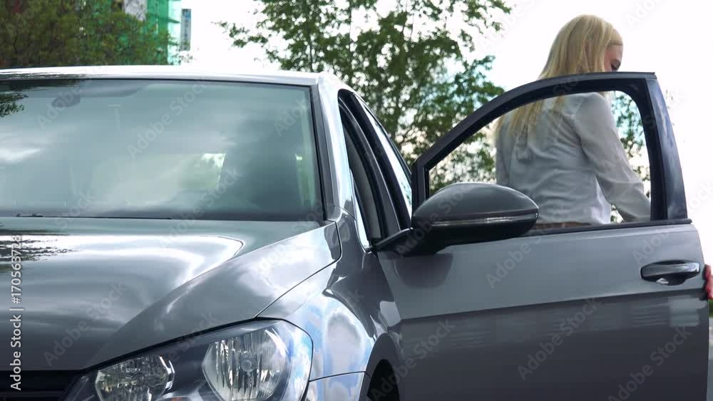 young attractive blond woman gets off the car and closes the door on the street with trees