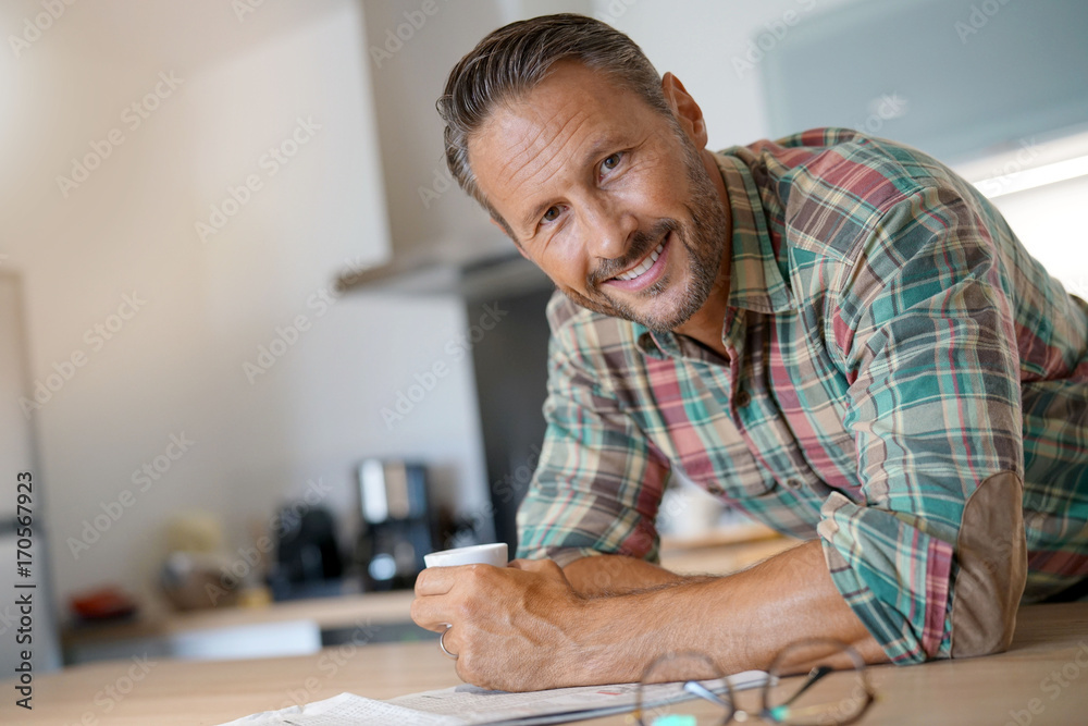 Smiling mature man drinking coffee and reading newspaper Smiling mature man drinking coffee and reading newspaper