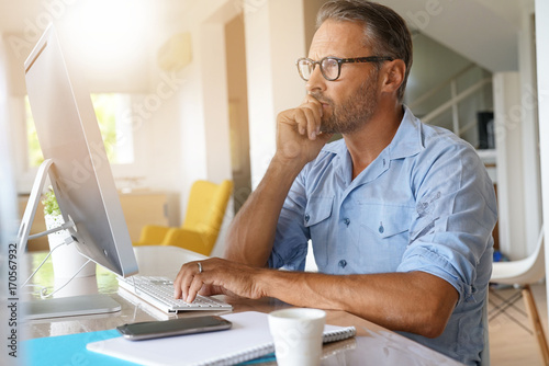 Mature man working from home on desktop computer photo