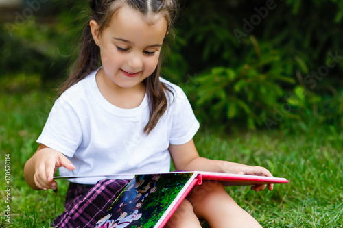 Little girl reads book lying on the green grass in the summer park photo