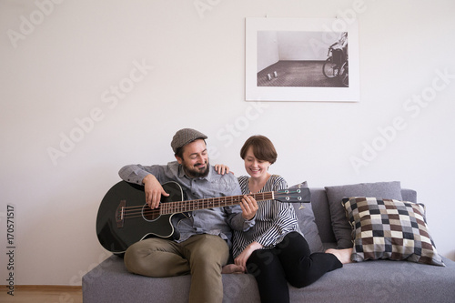 A young man is rehearsing on a bass guitar while the girlfriend is admiring him photo