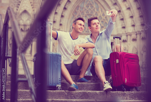 Two guys with luggage  taking selfie in city at summer day
