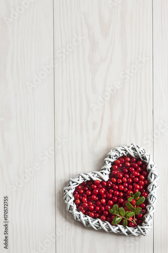  Fresh red forest cowberry in the shape of heart on a white wooden background. Concept for Christmas, Valentine's Day. Background, space for text, copy space