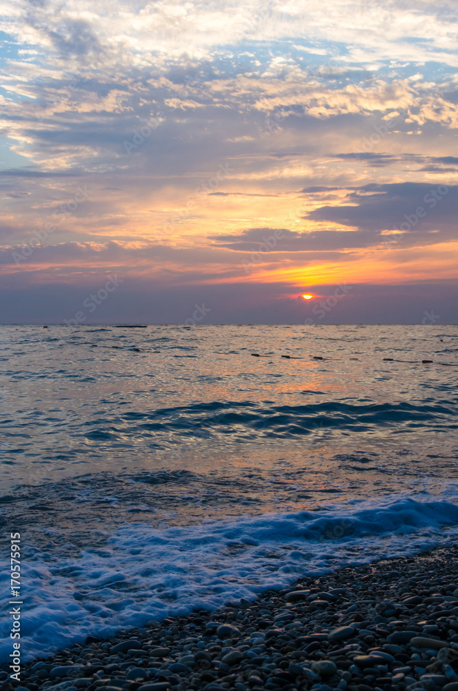 Obraz premium Amazing sea sunset on the pebble beach, the sun, waves, clouds