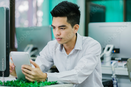 Portrait of handsome young businessman thinking project with tablet and computer at office. Asia people businessman.