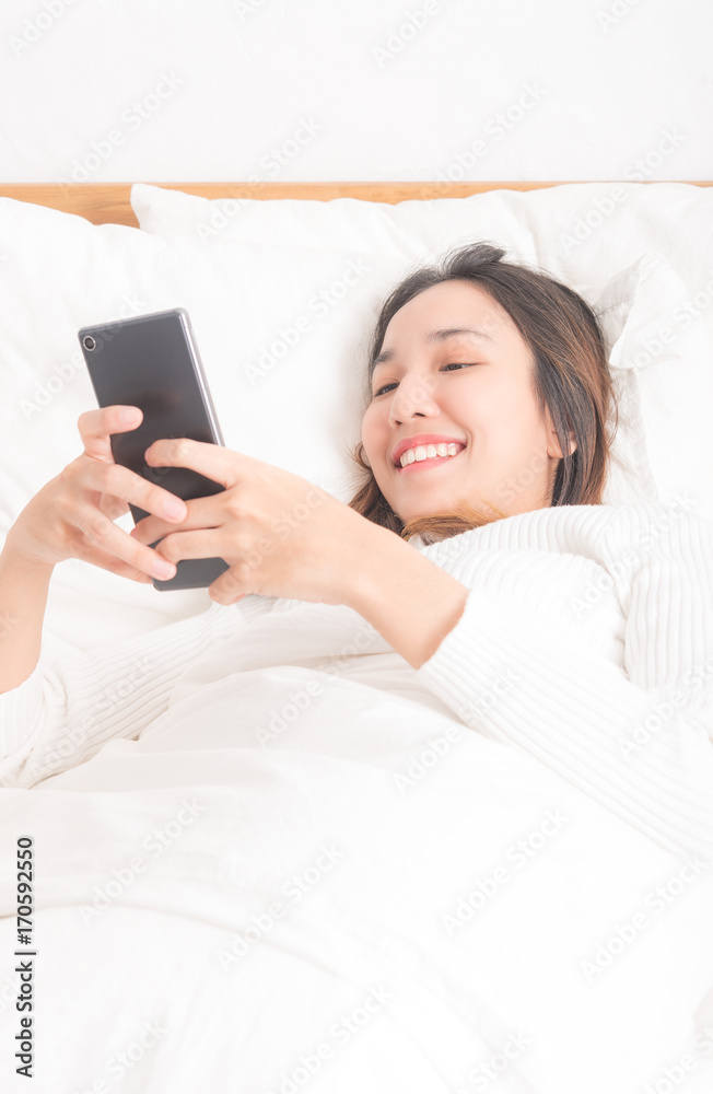 Happy female teenager Beautiful women are using cell phones, lying on the bed against white background Happy female teenager Beautiful women are using cell phones, lying on the bed against white background