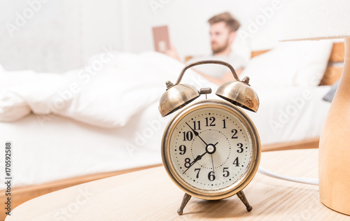 Vintage gold alarm clock in bedroom ,background is blurred of man waking up, on morning time. lifestyle at home and decorate concept