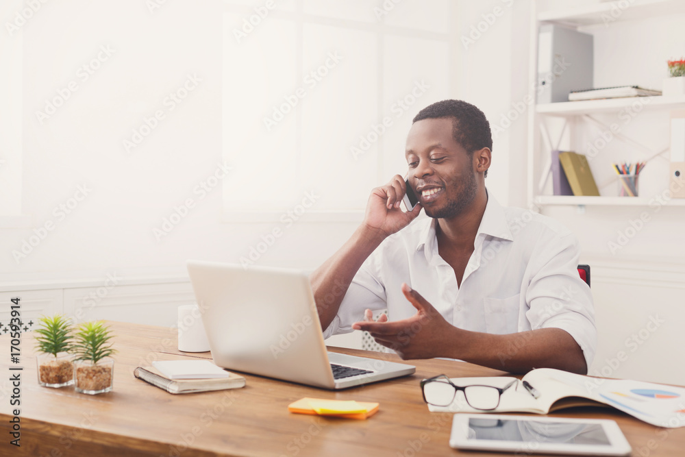 Young black businessman talking on mobile in modern white office