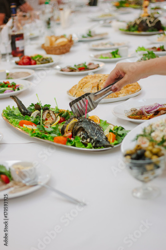 Hand with tongs keeping pieces of fish during banquet.