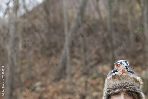 View of half young woman wearing winter hat and leaves. Cropped. Soft focus. Background