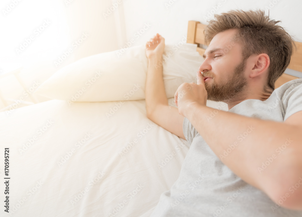 Handsome man waking up on bed in morning time.He putting fingers on lips as if to say shhh.sign mean Do not Disturb.lifestyle