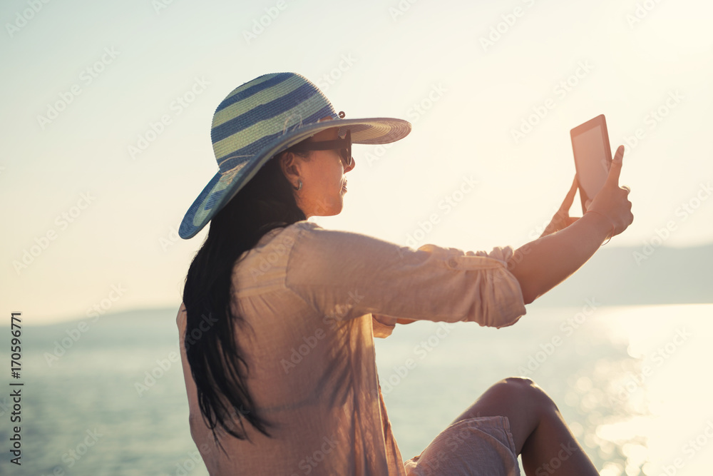 Smiling young woman take a selfie photo with digital tablet on the sea