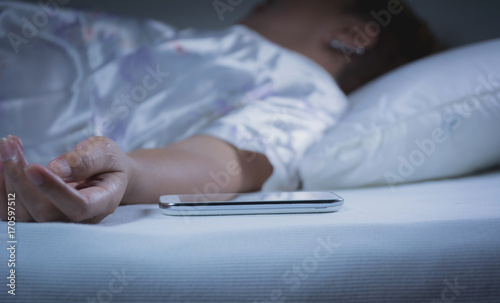 Woman sleeping with a mobile phone on the bed in bedroom, she is resting with eyes closed.