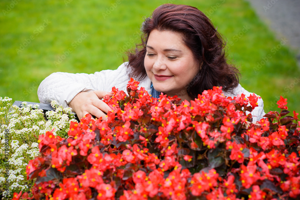 A mature American woman at an exhibition of flowers enjoys good weather and a wonderful mood. Lady size plus walks surrounded by greenery and flowers