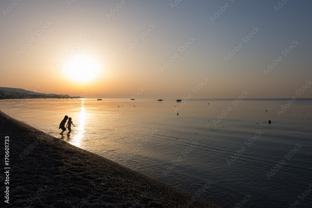 Close-up of little girls playing in the sea water at sunrise. Children's silhouette playing in golden hour.