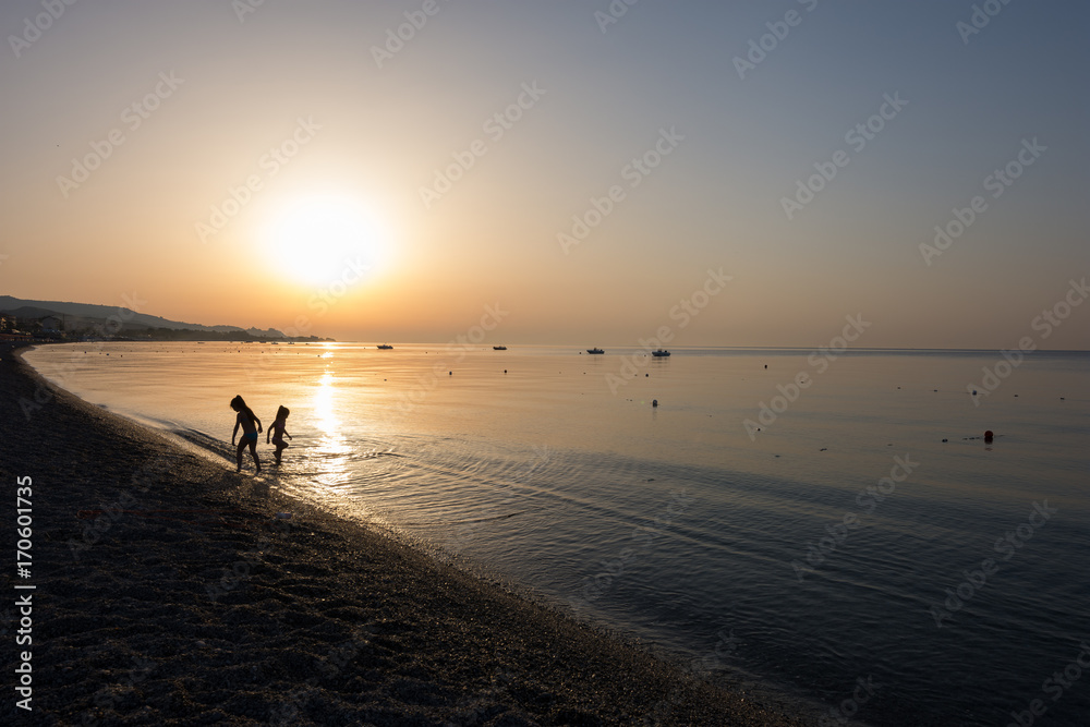 Close-up of little girls playing in the sea water at sunrise. Children's silhouette playing in golden hour.