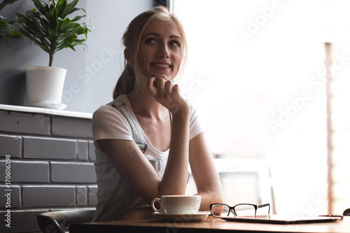 Starting new day in cafe. Side view of young attractive woman looking away while sitting in cafe with the cup of coffee.